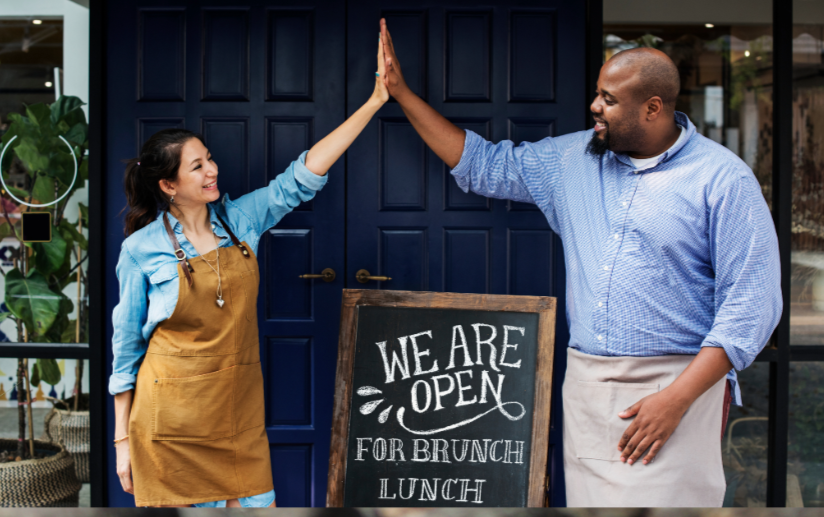 People high fiving in front of a sign that says we are open